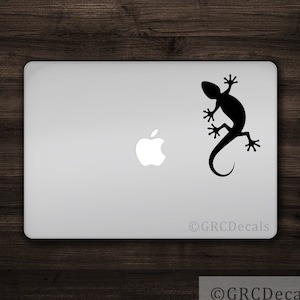 Może przedstawiać: Czarna naklejka z sylwetką gekona na srebrnym laptopie. Naklejka znajduje się po prawej stronie laptopa, nad logo Apple.
