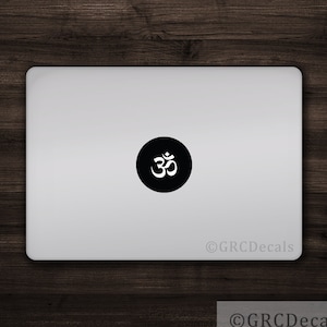 May include: A white Om symbol sticker on a black circle, placed on a silver laptop. The sticker is a popular symbol of peace and spirituality.