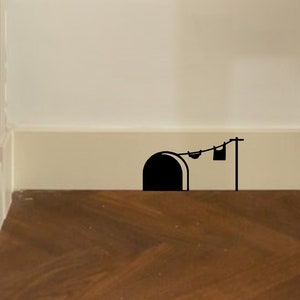 May include: A black mouse hole sticker on a white wall with a clothesline and laundry hanging above it.