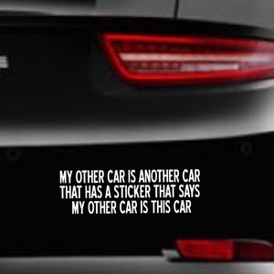 以下が含まれることがあります： 黒い車に、白いバンパーステッカーが貼ってあり、「私のもう一台の車は、私のもう一台の車がこの車であると書いてあるステッカーが貼ってある別の車です。」と書かれています。