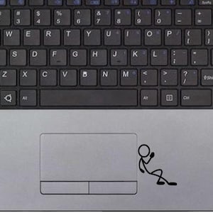 Op de afbeelding: Bovenaanzicht van een zilveren laptop met een zwart toetsenbord. Het toetsenbord heeft witte letters en cijfers. Een zwart stokfiguur zit op het touchpad. De laptop staat op een wit oppervlak.