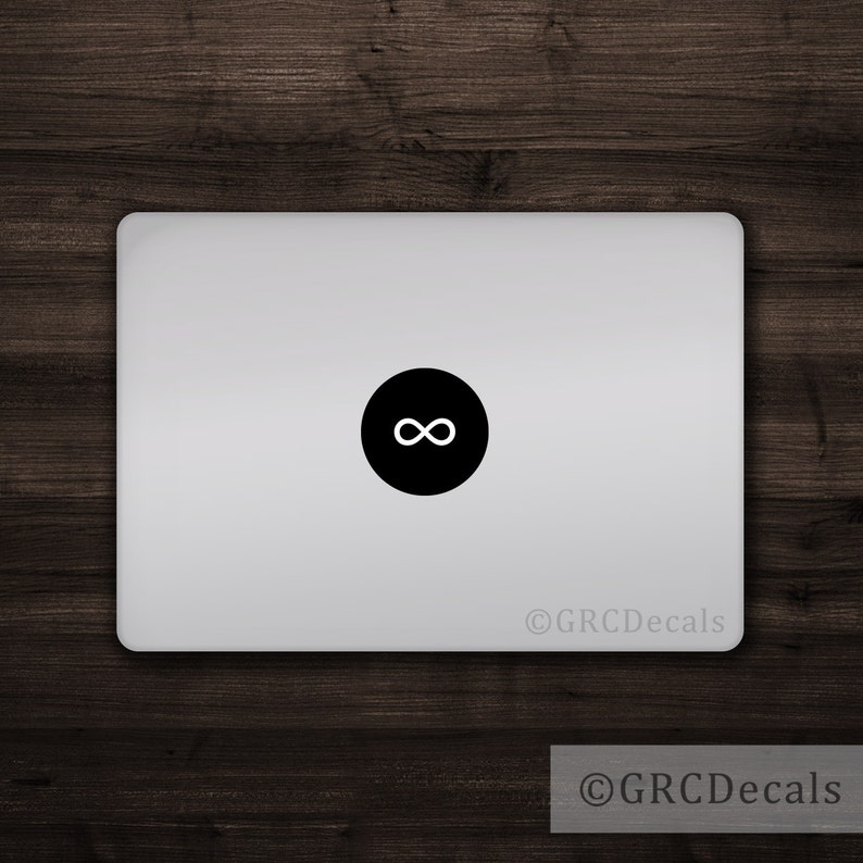 May include: A silver laptop with a black circle sticker featuring a white infinity symbol. The sticker is centered on the laptop's lid. The background is a dark wood grain.