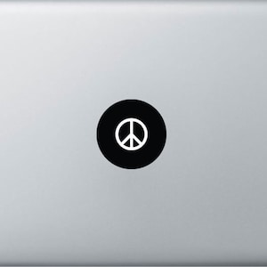 Puede incluir: Una pegatina de signo de paz en blanco y negro en una computadora portátil plateada.