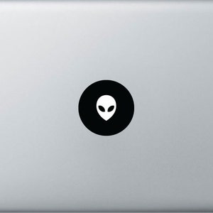 Könnte beinhalten: Ein schwarzer Kreisaufkleber mit einem weißen Alienkopfdesign auf einem silbernen Laptop.