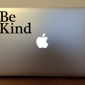 May include: A silver laptop computer with a black sticker that says "Be Kind" on the top left corner. The Apple logo is visible on the lid.