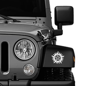 May include: A close-up of a gray Jeep's front end, featuring a white decal of a sunburst with a pentagram in the center. The Jeep has a black bumper and a round headlight.