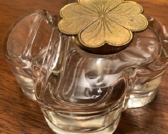 May include: A clear glass inkwell with a decorative, gold-colored, clover-shaped lid. The inkwell has a wavy, textured surface.