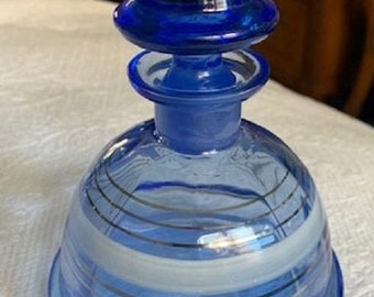 May include: A cobalt blue glass bottle with a white and silver striped design. The bottle has a unique, layered, dome-shaped stopper.