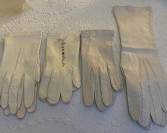 May include: Four pairs of white leather gloves. Two pairs are short and one pair has embroidered flowers. One pair is long.