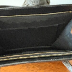 May include: Open view of a black leather wallet with a gold zipper. The interior of the wallet is black with multiple compartments. The wallet is open, revealing the inside.