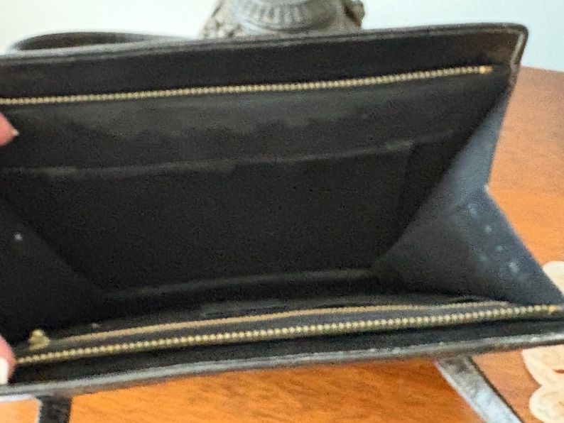 May include: Open view of a black leather wallet with a gold zipper. The interior of the wallet is black with multiple compartments. The wallet is open, revealing the inside.