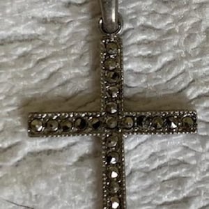 May include: A silver cross pendant with a detailed design of small, sparkling stones.