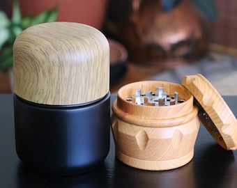 May include: A wooden grinder with a black and wood lid, and a separate black and wood container. The grinder has a metal grinding mechanism.