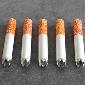 May include: Five white and orange cigarette-shaped pipes with a serrated metal tip.