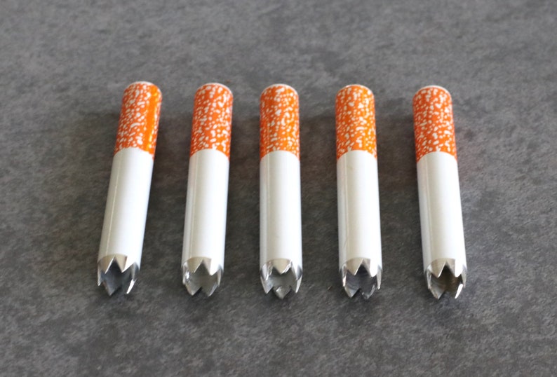 May include: Five white and orange cigarette-shaped pipes with a serrated metal tip.