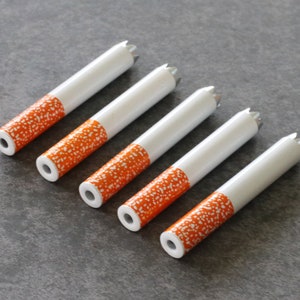 May include: Five white cigarette-shaped tubes with orange and white speckled designs. The tubes have a pointed end and a flat end.