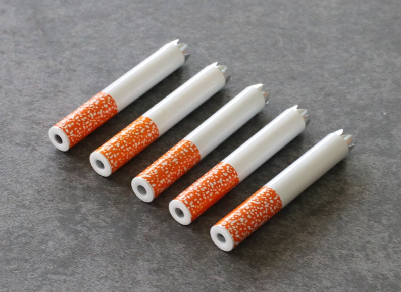 May include: Five white cigarette-shaped tubes with orange and white speckled designs. The tubes have a pointed end and a flat end.