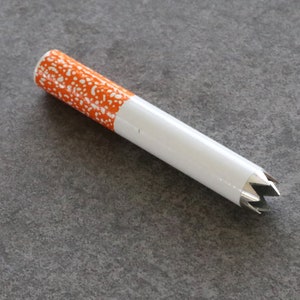May include: A white and orange cigarette-shaped pipe with a star-shaped metal tip.