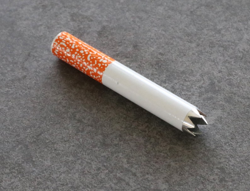 May include: A white and orange cigarette-shaped pipe with a star-shaped metal tip.