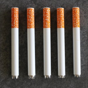 May include: Six white metal cigarette tubes with orange and white patterned tips.