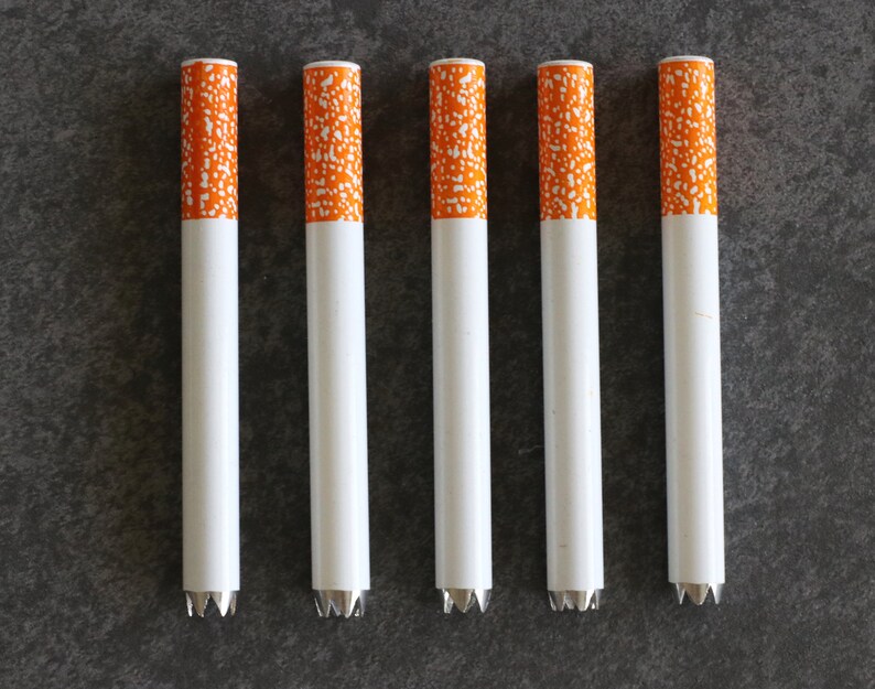 May include: Six white metal cigarette tubes with orange and white patterned tips.