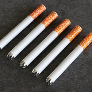 May include: Five white cigarette-shaped tubes with orange tips and silver pointed ends. The tubes are arranged in a row, with the tips facing the viewer.