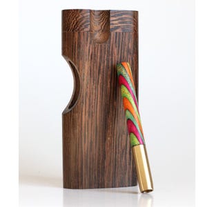 May include: A wooden dugout with a curved cutout and a colorful, patterned one-hitter pipe. The dugout is made of dark brown wood with a natural grain. The pipe features a brass tip and a vibrant swirl of colors including red, green, orange, and yellow.