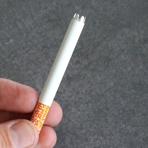 May include: A white cigarette with an orange and white patterned tip. The cigarette is partially crushed at the end.