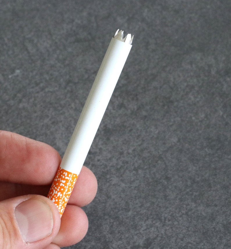 May include: A white cigarette with an orange and white patterned tip. The cigarette is partially crushed at the end.