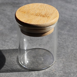 May include: A clear glass jar with a bamboo lid. The lid has a white ring around the edge.