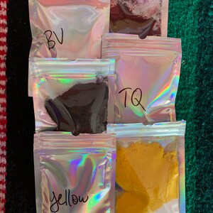 May include: Five small clear plastic bags with zippers, each containing a different colored powder. The bags are labeled "BV", "TQ", "Yellow", and two are unlabeled.