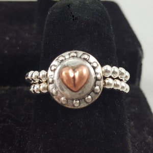 May include: A silver ring with a beaded band and a round centerpiece featuring a copper heart.