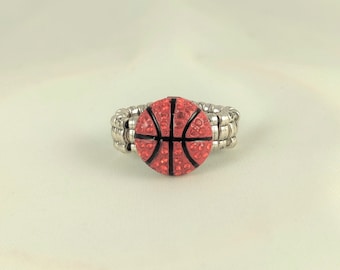 May include: A silver adjustable ring with a red and black basketball design. The basketball is covered in rhinestones.
