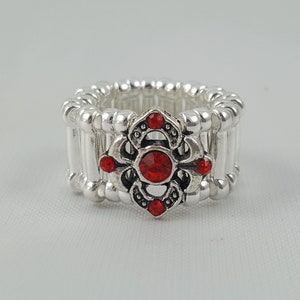 May include: Silver ring with a red rhinestone flower design. The ring is adjustable and has a simple, elegant style.