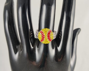 May include: A silver ring with a red and yellow baseball design. The baseball is covered in rhinestones.