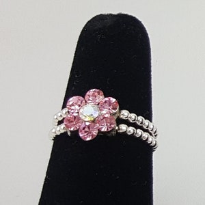 May include: A silver ring with a pink flower design. The flower has a clear center stone and is surrounded by smaller pink stones.