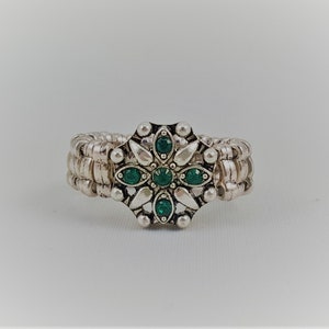 May include: A silver ring with a green jeweled flower design.