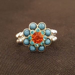 May include: A silver ring with a turquoise and orange flower design. The flower has a large orange center stone surrounded by smaller turquoise stones.