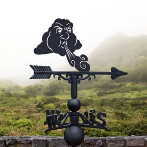 May include: Black metal weather vane featuring a cartoon cloud blowing wind. The cloud has a face with an angry expression. The vane is mounted on a wooden post and is set against a backdrop of green hills and fog.