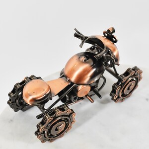 Puede incluir: Una peque&ntilde;a escultura de metal de color cobre de una motocicleta. La motocicleta est&aacute; hecha de varias piezas de metal, incluidas cadenas y engranajes. La escultura mide aproximadamente 13 cm de alto y 10 cm de ancho.