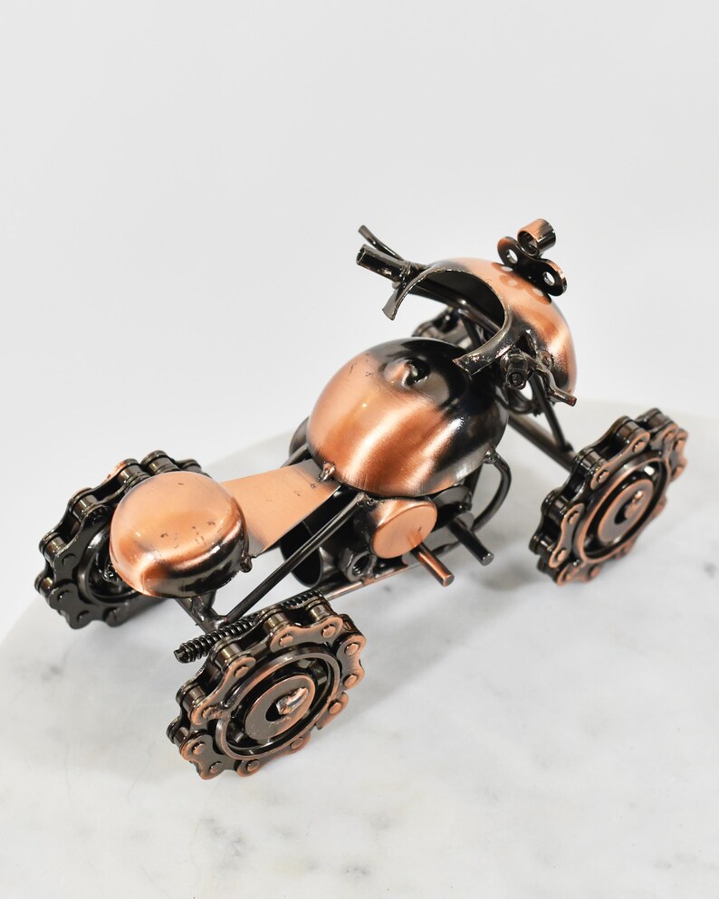 Puede incluir: Una peque&ntilde;a escultura de metal de color cobre de una motocicleta. La motocicleta est&aacute; hecha de varias piezas de metal, incluidas cadenas y engranajes. La escultura mide aproximadamente 13 cm de alto y 10 cm de ancho.