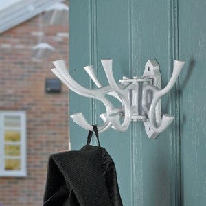 May include: A white metal coat rack with multiple curved hooks, mounted on a teal door. A black jacket hangs from one of the hooks. The rack has a decorative design, suitable for hallways or utility rooms.