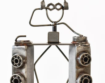May include: A metal sculpture depicting a DJ. The figure is constructed from metal components such as nuts, bolts, and bearings. The DJ wears headphones and has arms extended towards a mixing console.