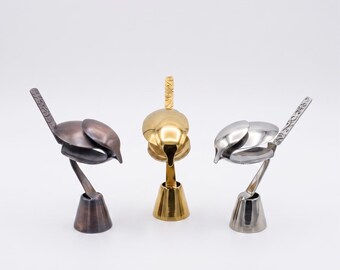 May include: Three bird-shaped sculptures crafted from metal spoons, each featuring a conical base, a curved body, and a long tail with embossed floral patterns. The sculptures are finished in metallic bronze, gold, and silver tones respectively.