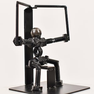 May include: A black metal sculpture of a person working out on a lat pulldown machine. The sculpture is made of nuts, bolts, and metal rods.