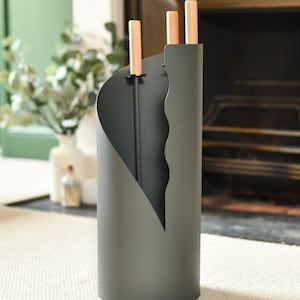 May include: A dark grey metal fireplace tool holder with a wavy design. The holder has three slots for tools, and the tools have wooden handles.