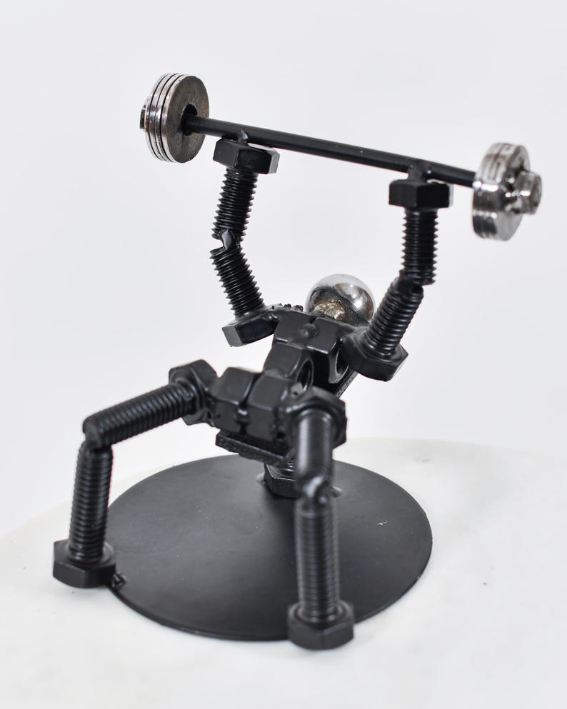 May include: A black metal sculpture of a person lifting weights. The sculpture is made of nuts and bolts and is on a black metal base.