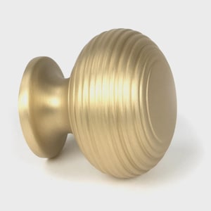 May include: A gold-toned cabinet knob with a round, ribbed design. The knob has a smooth, slightly domed top and a smaller, round base.