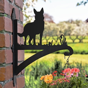 May include: Black metal silhouette of a German Shepherd dog mounted on a wall-mounted bracket with a hanging planter. The planter is filled with colourful flowers.