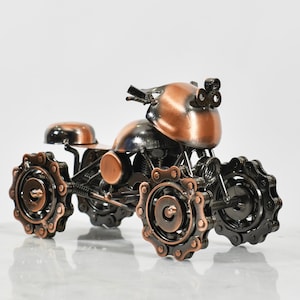 Puede incluir: Una peque&ntilde;a escultura de motocicleta de metal de color cobre con detalles negros. La motocicleta tiene cuatro ruedas hechas de cadenas unidas.